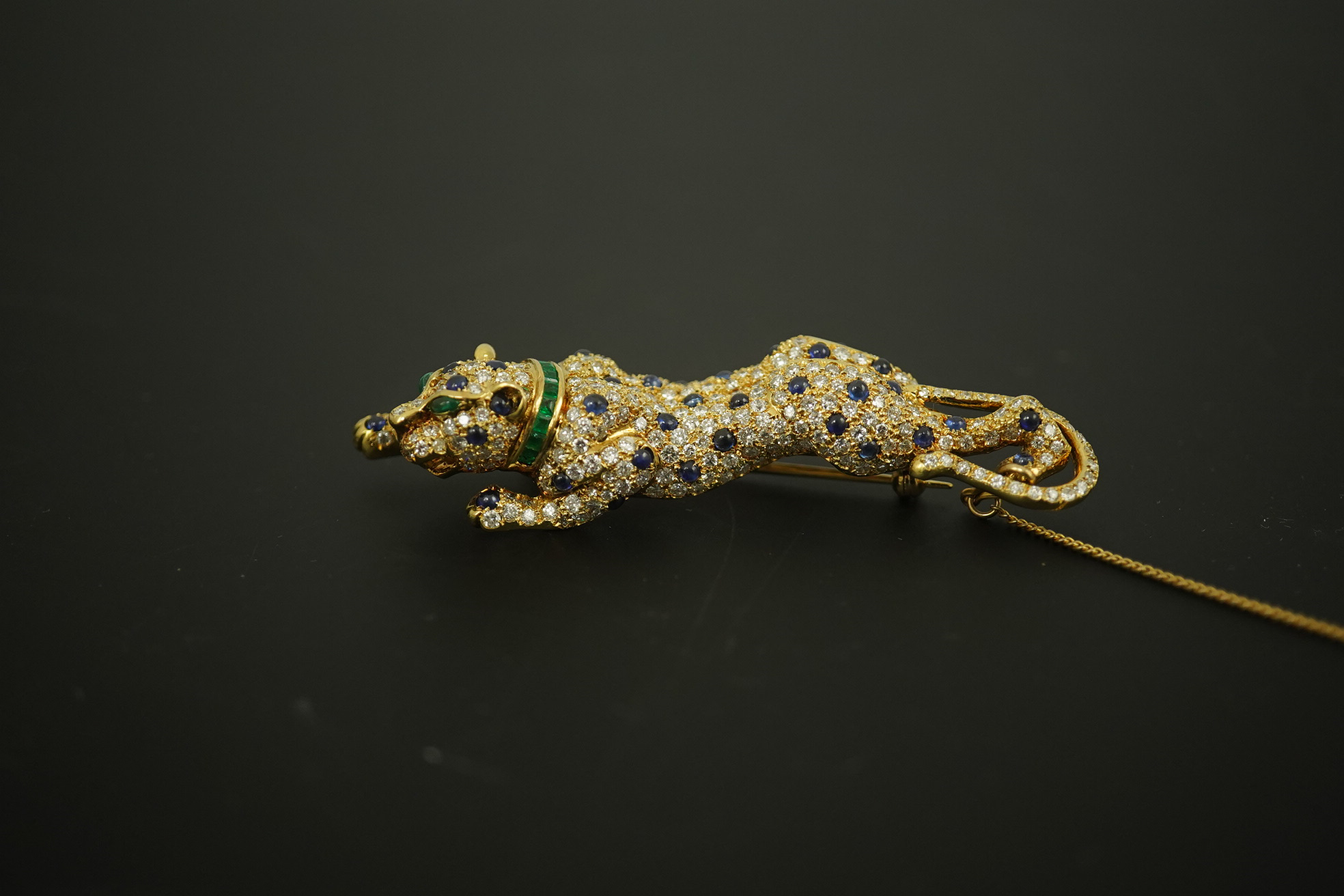 A modern Cartier style 18k gold, sapphire, emerald and diamond cluster set stalking panther brooch